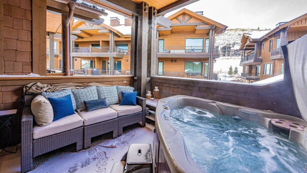 A cozy outdoor seating area with a hot tub, wooden furniture, and a view of a ski resort.