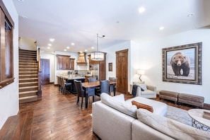 A spacious living area with a sofa, a dining table with chairs, a kitchen with wooden cabinets, and a staircase. - Juniper Landing (Park City)