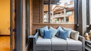 A wicker sofa with cushions, a glass table, and a view of a building with balconies.