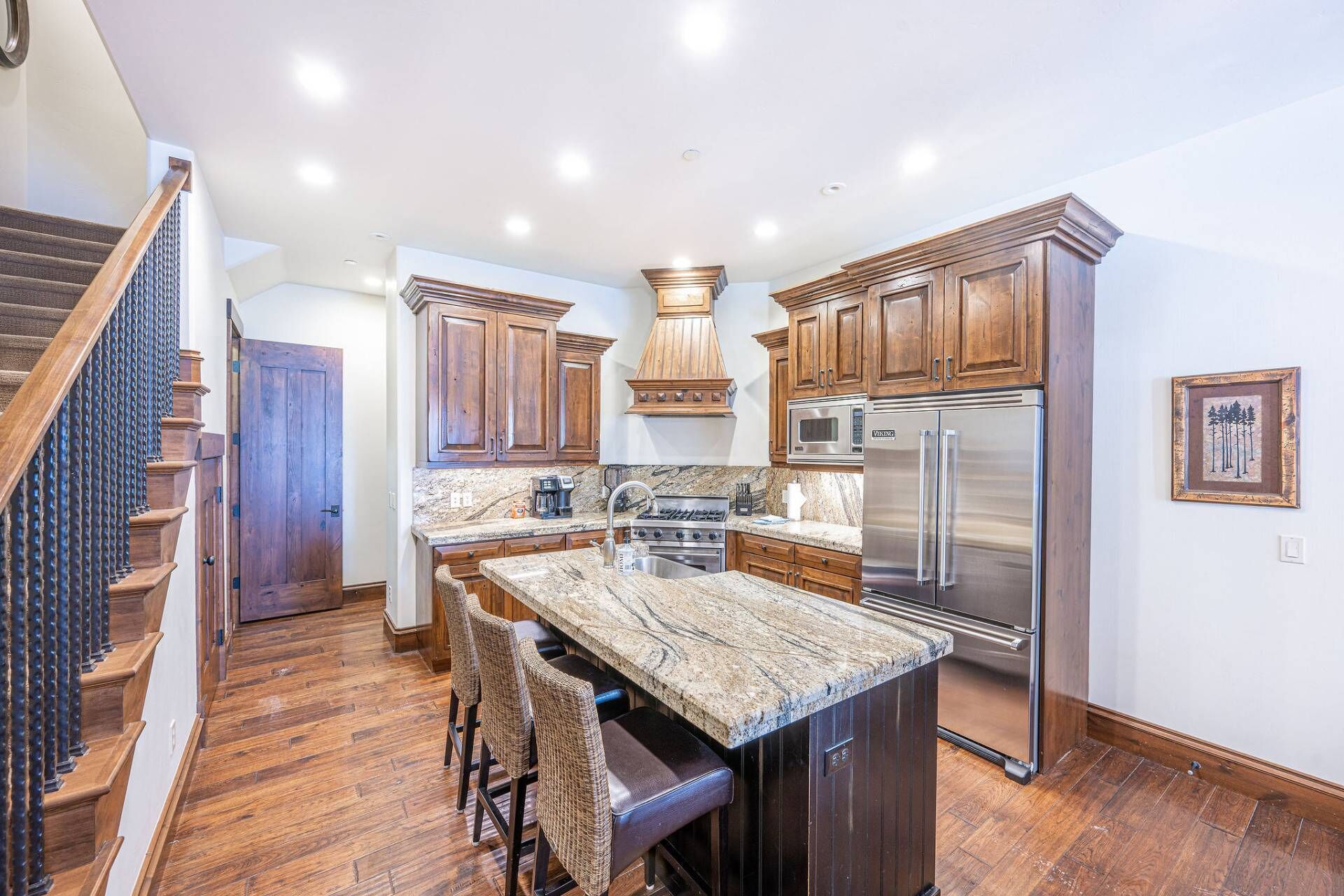 A kitchen with wooden cabinets, a granite countertop, a stainless steel refrigerator, and a built-in stove.