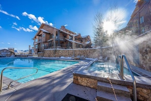 A resort with a swimming pool, a hot tub, and a stone wall.