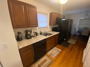 Kitchen area with a dishwasher, coffee maker, and sink, adjacent to a dining space with a table and chairs.