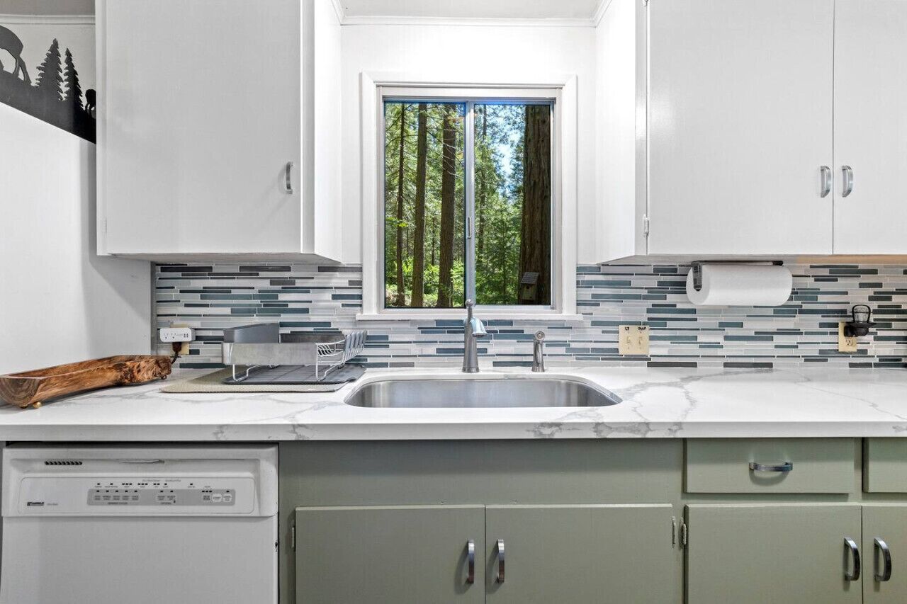 A modern kitchen with a large window, a built-in dishwasher, and a tiled backsplash.