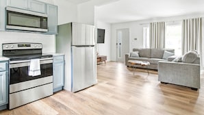 A modern kitchen with stainless steel appliances, a grey sofa, and a wooden floor. - Fully remodeled Cozy house, 10 min. from airport (Irving)