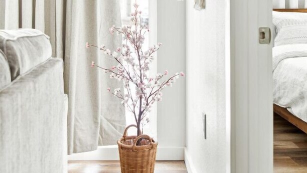 A room with a bed, a window with curtains, a wall-mounted macrame piece, and a basket with flowers. - Fully remodeled Cozy house, 10 min. from airport (Irving)