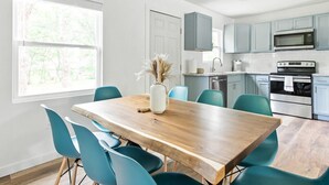 A modern kitchen with light blue cabinets, a wooden dining table, and teal chairs. - Fully remodeled Cozy house, 10 min. from airport (Irving)