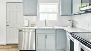 A kitchen with light blue cabinets, a stainless steel dishwasher, a white countertop, and a window above the sink. - Fully remodeled Cozy house, 10 min. from airport (Irving)
