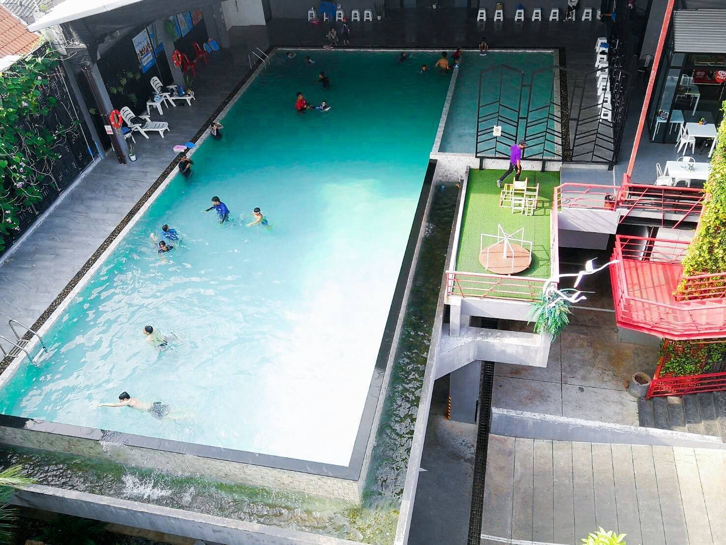 An indoor swimming pool with multiple lanes, a diving platform, and a seating area with chairs and tables.