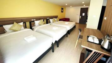 A hotel room with three beds, a wooden headboard, a dining table with a kettle, and a red chair.