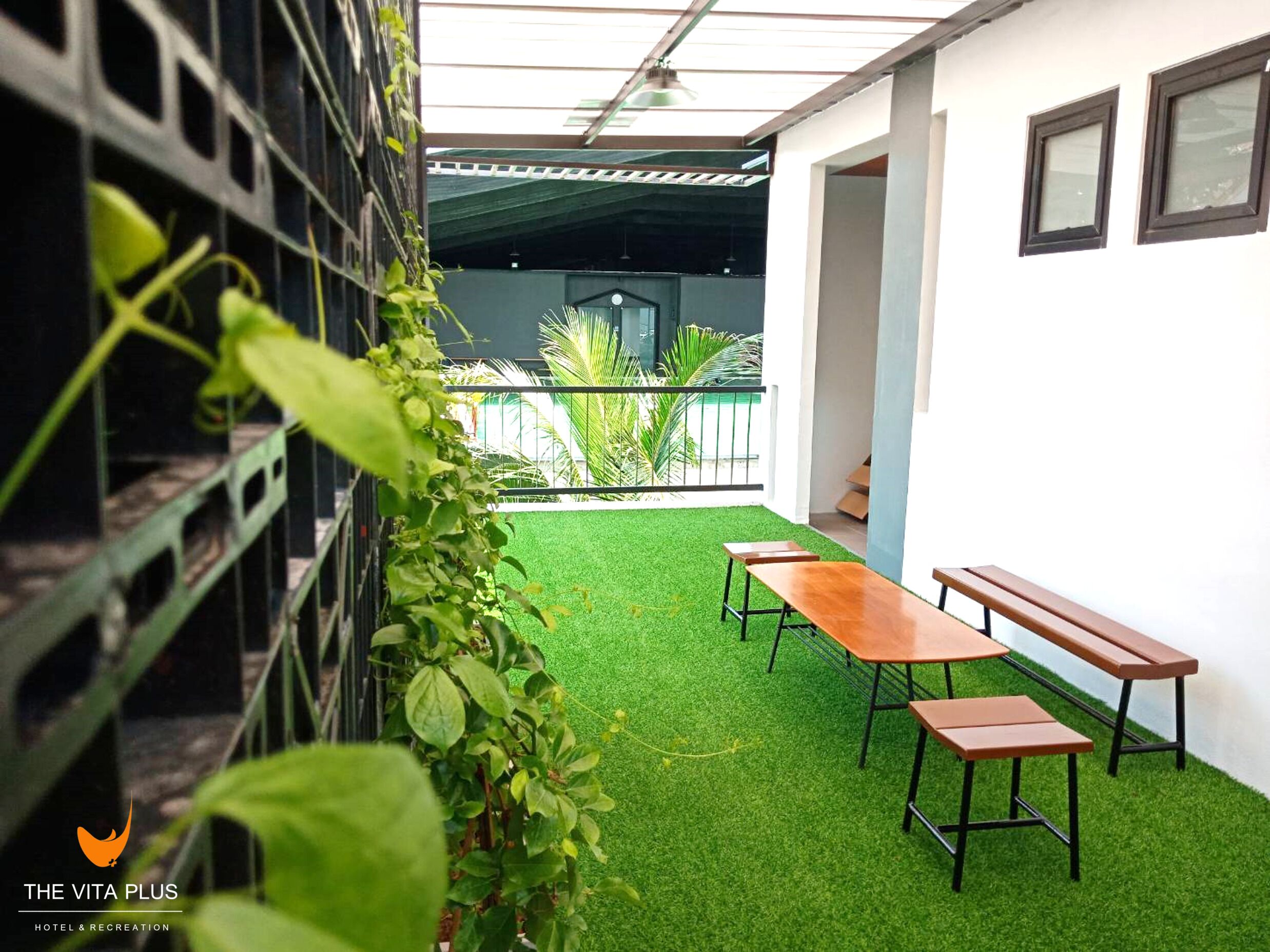 Un patio interior con césped artificial, bancos de madera y una valla de metal.
