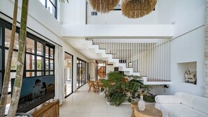 A spacious, modern living area with a staircase, a flat-screen TV, and a white sofa. - Rumah Simba (Munggu)