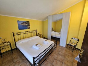 A bedroom with a bed, a bedside table, a chair, a mirror, and a painting on the wall.