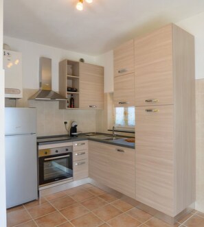 A compact kitchen with a built-in oven, a coffee maker, and light wood cabinetry.