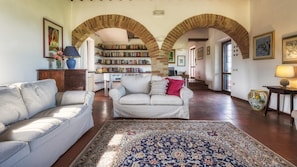 Uma sala de estar espaçosa com um sofá branco, um tapete estampado e uma estante repleta de livros.