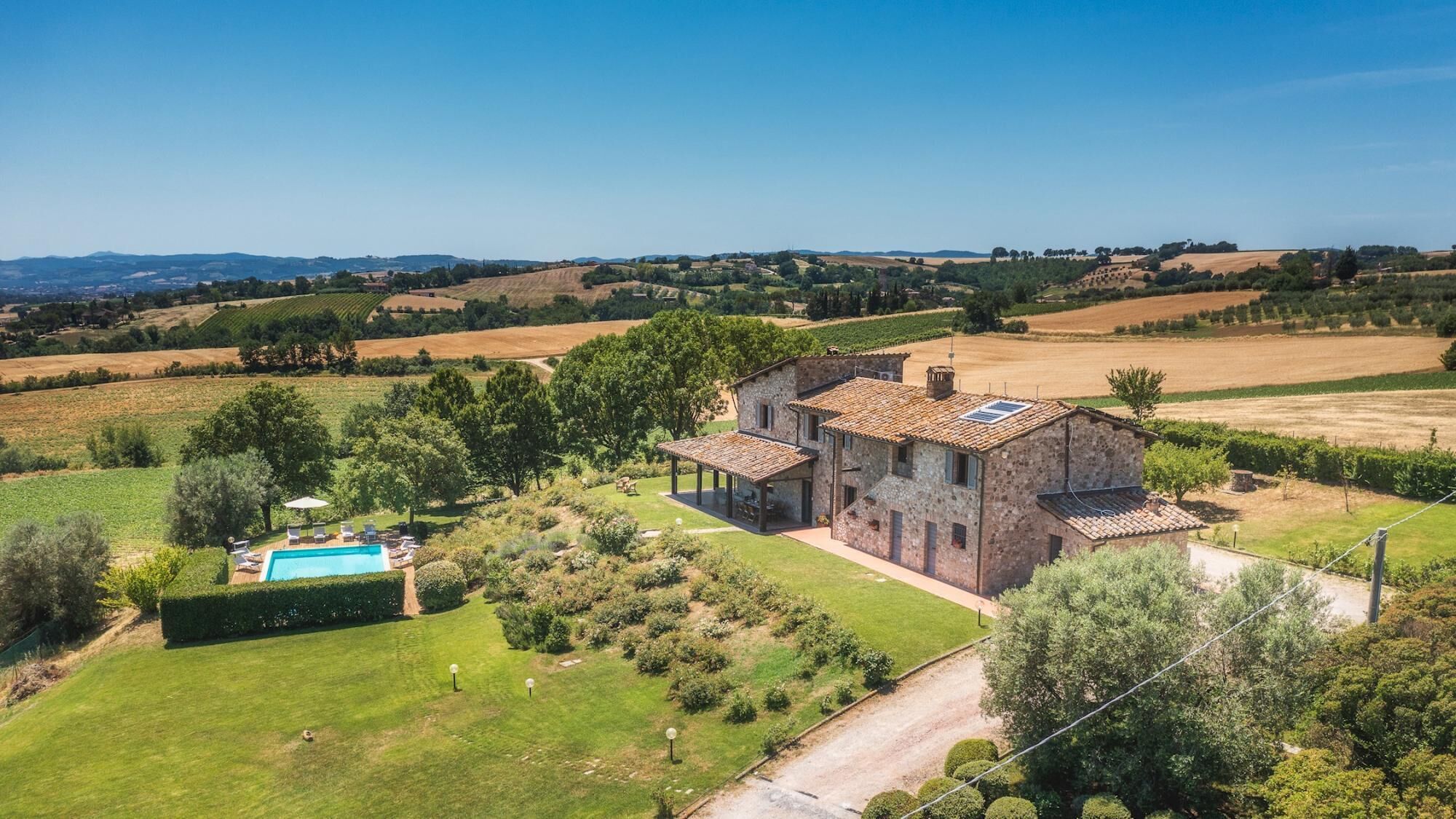 A stone villa with a swimming pool, surrounded by lush greenery and fields.