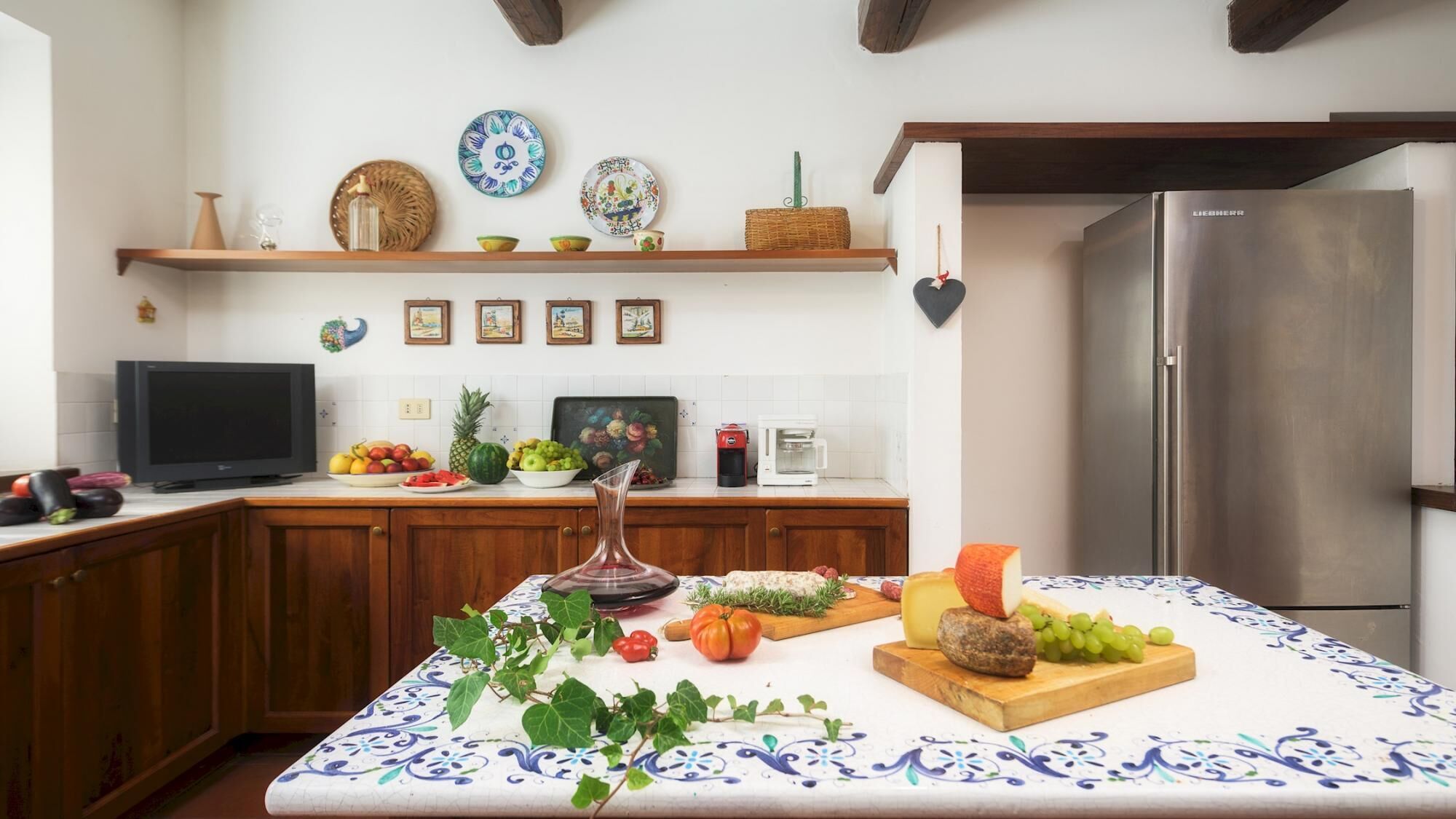 A kitchen with wooden cabinets, a stainless steel refrigerator, a coffee maker, and a variety of fruits and vegetables on the counter.
