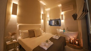 A hotel room with a large bed, a vanity with a bathtub, and a small table with a vase of flowers. - Donna Lucia Romantic Villa w/ jacuzzi Sea Front (Monopoli)