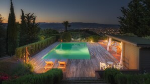 A swimming pool with lounge chairs and a small building with a roof, surrounded by trees and a view of a cityscape at dusk. - Villa Marraccini 8 in Lucca (Lucca)