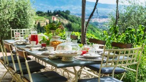 An outdoor dining table set with chairs, surrounded by greenery and a scenic view. - Villa Marraccini 8 in Lucca (Lucca)