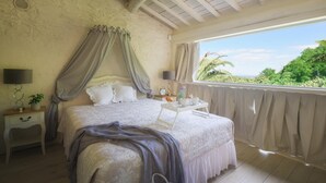 A bedroom with a bed, a nightstand, a bedside table, and a window with a view of greenery. - Villa Marraccini 8 in Lucca (Lucca)