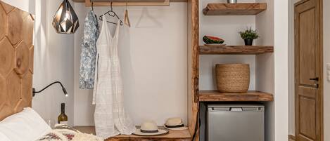A bedroom with a bed, a hanging light, a wooden shelf with plants, and a small table with a hat and bottle.