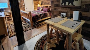 Un intérieur rustique avec un lit en bois, une table à manger avec des sets de table, une décoration murale sur le thème des ours et un tapis à motifs.