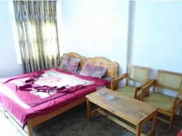 Une chambre à coucher avec un lit, deux chaises, une petite table et une fenêtre avec des rideaux.