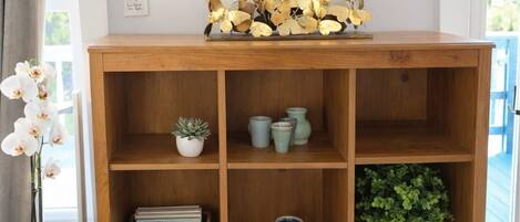Una consola de madera con varios estantes, un espejo redondo y elementos decorativos, incluyendo una planta y una cesta de toallas.