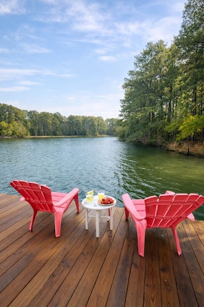 Een houten terras met twee rode Adirondack-stoelen en een tafeltje met een drankje en fruit.