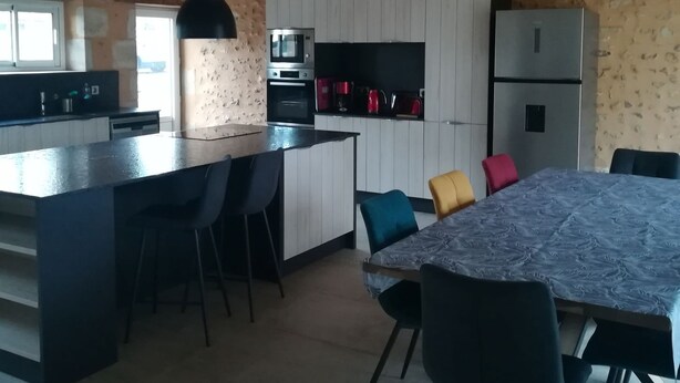 Una cuina moderna amb armaris blancs, una illa central amb tamborets i una zona de dinar amb mantell estampat.