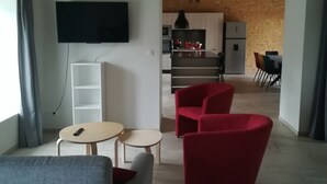 Un saló modern amb un sofà gris, un butàquim vermell i una taula rodona petita. Un televisor de pantalla plana està fixat a la paret.