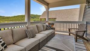 Uma área de estar coberta ao ar livre com sofá, cadeiras, uma mesa e vista para uma paisagem montanhosa.