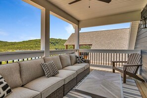 Un espace extérieur aménagé, abrité et doté d’un canapé et de fauteuils, d’une table, et offrant une vue sur un paysage vallonné.