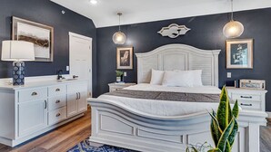 Quarto com cama branca, penteadeira e mesa de cabeceira.