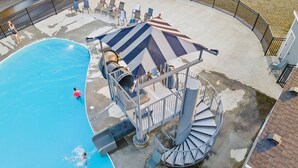 Piscina com escorregador e escadaria em espiral que dá acesso a um deck.