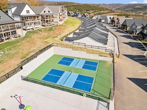 Ein Tennisplatz mit umgebendem Zaun, neben einer Reihe von Häusern mit geneigten Dächern.