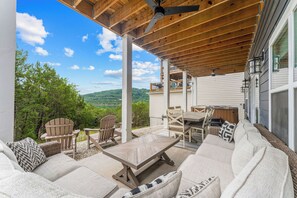 A covered outdoor seating area with Adirondack chairs, a wooden table, and a sofa.