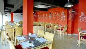 A restaurant with wicker furniture, red walls, and white line drawings of people. - Hotel Siri Inn (Hyderabad)