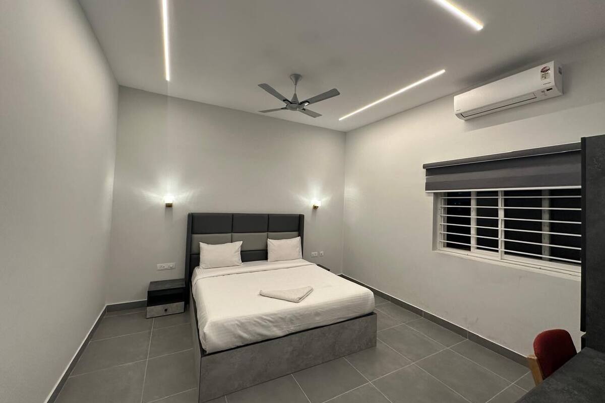 A modern bedroom with a bed, bedside tables, a ceiling fan, an air conditioning unit, and a window with blinds.
