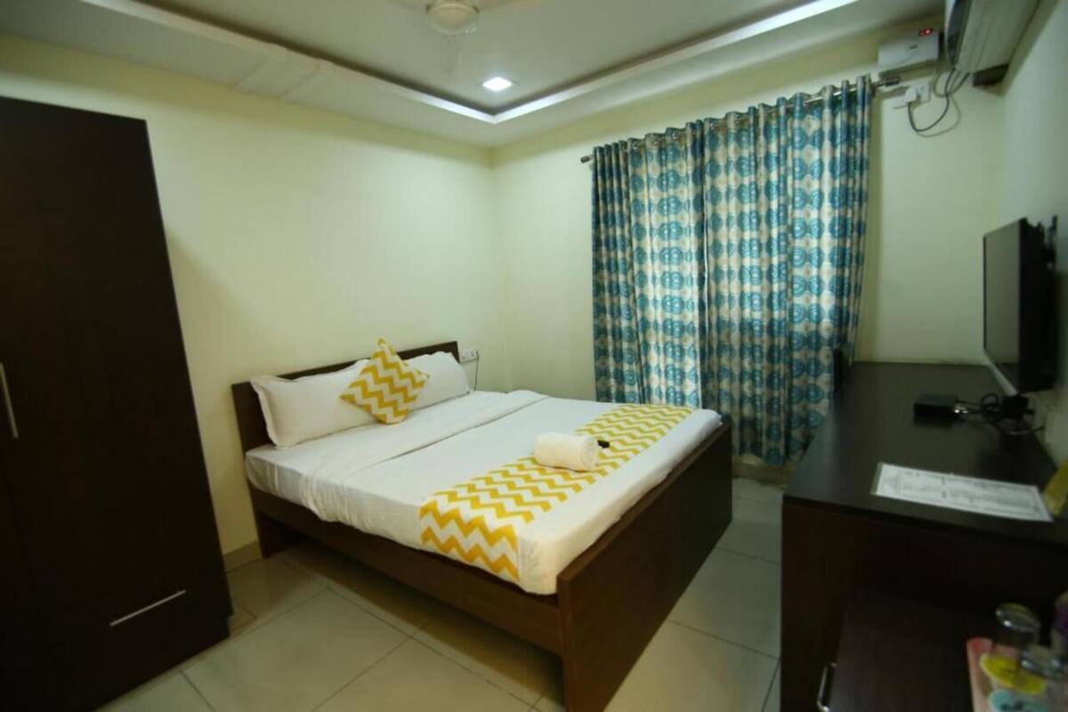 Quarto com cama, escrivaninha, televisão e cortinas.