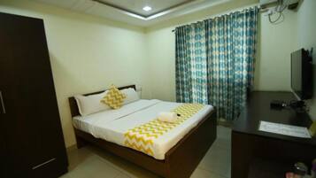 A bedroom with a bed, a desk, a television, and curtains.