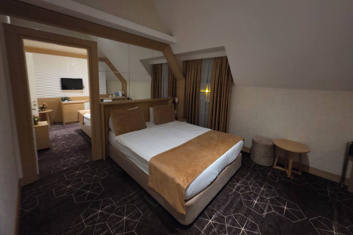 A hotel room with a large bed, a desk, a chair, a small table, and a TV mounted on the wall.