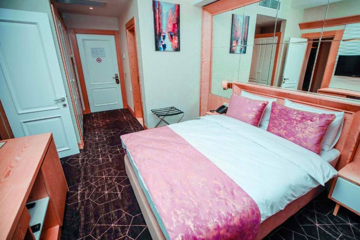 A bedroom with a bed, a desk, a chair, a wardrobe, and a mirror.
