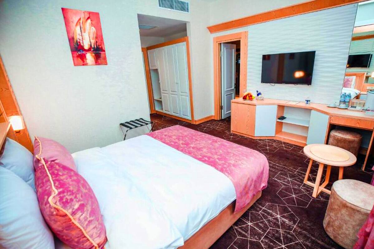 A hotel room with a bed, a desk, a chair, a TV, and a mirror.