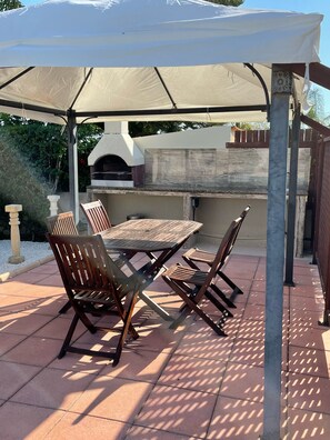 Eine Außenpatio mit Tisch und Stühlen, einer Pergola und einem Steinofen.