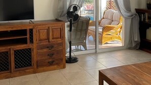 A living room with a wooden TV stand, a fan, and a view of a balcony with wicker furniture. - Coral Bay Bungalow (Coral Bay)