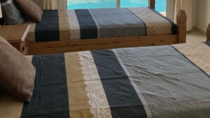 A bedroom with a large bed, two pillows, a wooden headboard, and a view of a pool and beach through a sliding door. - Coral Bay Bungalow (Coral Bay)