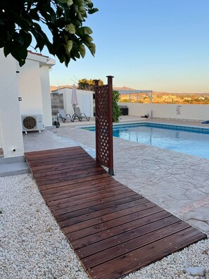 Ein Poolbereich mit Holzterrasse, einem weißen Gebäude und Blick auf ferne Hügel.