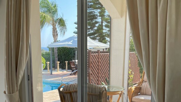 A room with a glass door leading to a pool area, wicker furniture, and a white table with a vase. - Coral Bay Bungalow (Coral Bay)