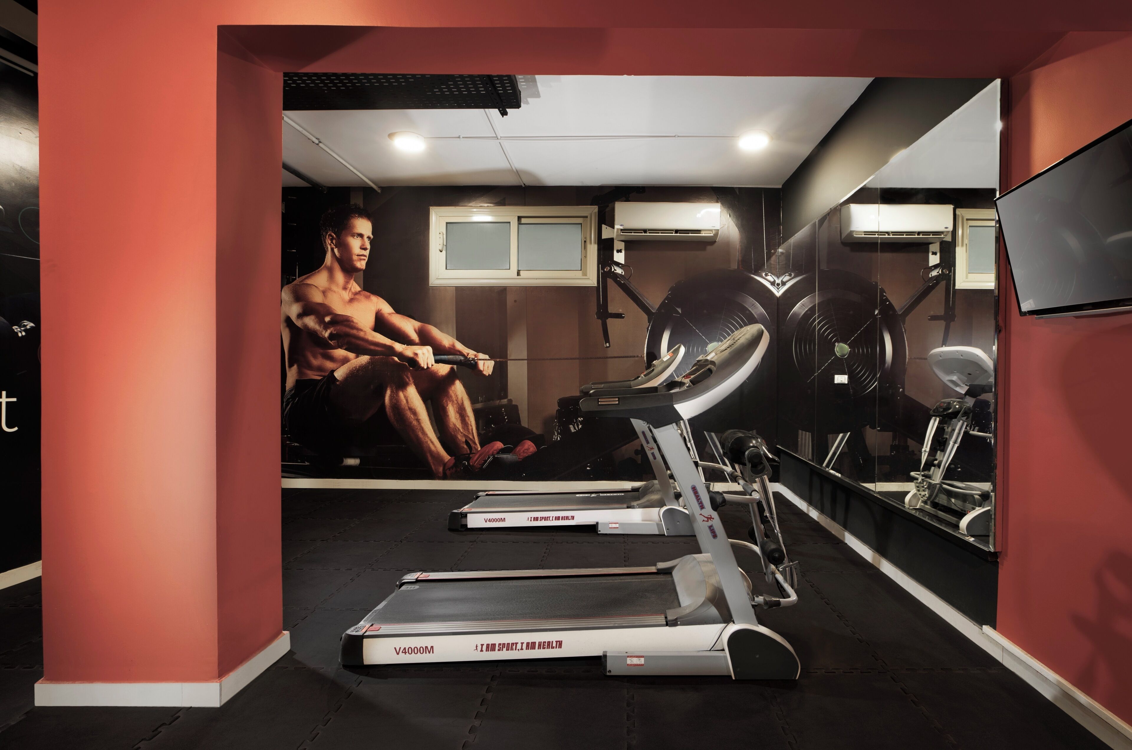 Een sportschool met loopbanden, een hometrainer en een grote spiegel.